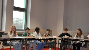 Uczestnicy konkursu siedzą przy stolikach w sali konferencyjnej i zastanawiają się nad odpowiedzią na pytanie