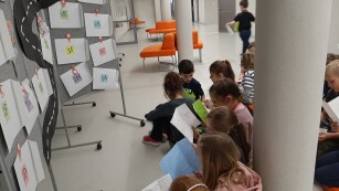 Uczniowie czytają komiks wykonany przez uczniów klasy 3 na tle tablicy z napisem - Podróże po literaturze.
